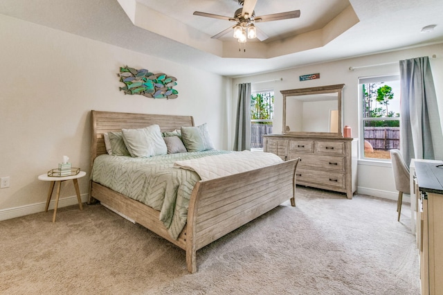 bedroom featuring ceiling fan, a tray ceiling, and light colored carpet