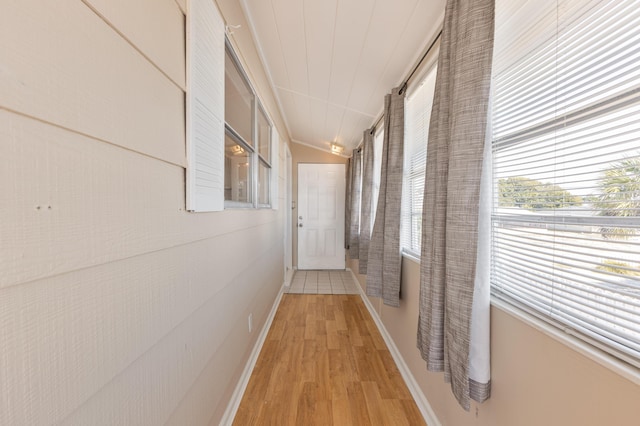 hallway featuring light wood-type flooring, vaulted ceiling, and baseboards