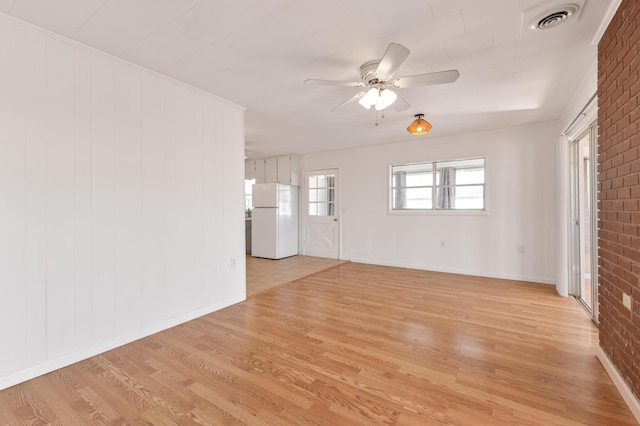 unfurnished room featuring visible vents, light wood-style flooring, ceiling fan, brick wall, and baseboards