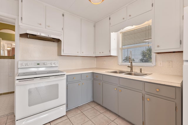 kitchen with light tile patterned floors, under cabinet range hood, a sink, gray cabinets, and white range with electric cooktop