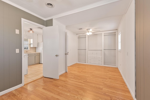 empty room featuring a ceiling fan, baseboards, visible vents, light wood-type flooring, and crown molding