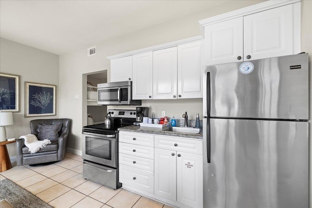 kitchen with appliances with stainless steel finishes, white cabinetry, sink, dark stone counters, and light tile patterned floors