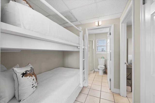 bedroom featuring ensuite bath, a drop ceiling, and light tile patterned floors