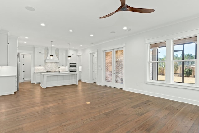 unfurnished living room featuring wood-type flooring, sink, ceiling fan, crown molding, and french doors