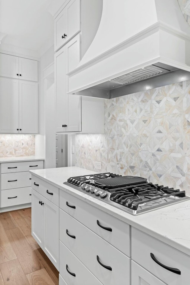 kitchen featuring decorative backsplash, custom range hood, white cabinets, and stainless steel gas cooktop