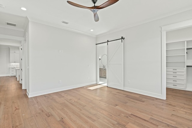 unfurnished bedroom featuring a spacious closet, ornamental molding, a barn door, and ceiling fan