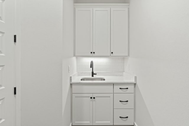 bar featuring white cabinetry, sink, and backsplash