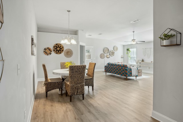 dining space featuring ceiling fan with notable chandelier, vaulted ceiling, and light wood-type flooring