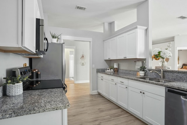 kitchen with sink, light hardwood / wood-style flooring, dark stone counters, stainless steel appliances, and white cabinets