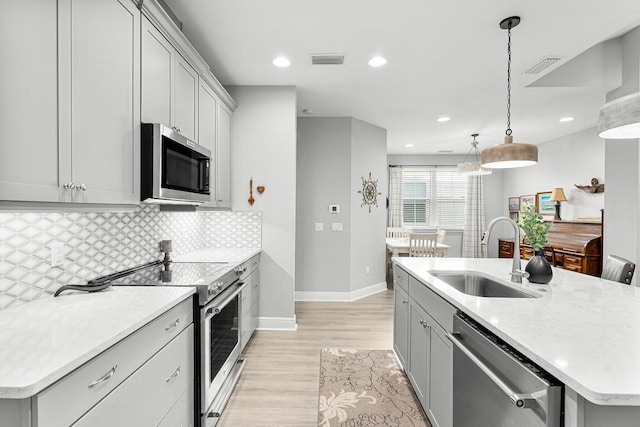 kitchen featuring stainless steel appliances, sink, pendant lighting, and a kitchen island with sink