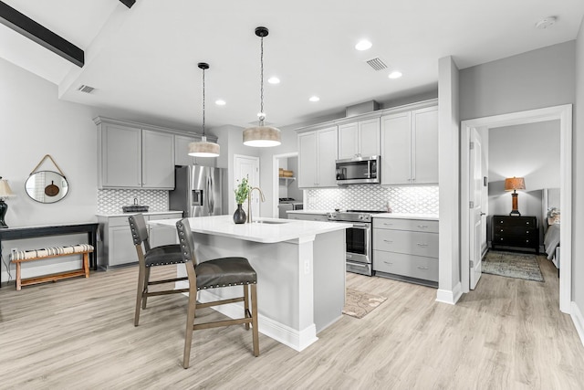 kitchen featuring a breakfast bar area, appliances with stainless steel finishes, gray cabinets, an island with sink, and pendant lighting