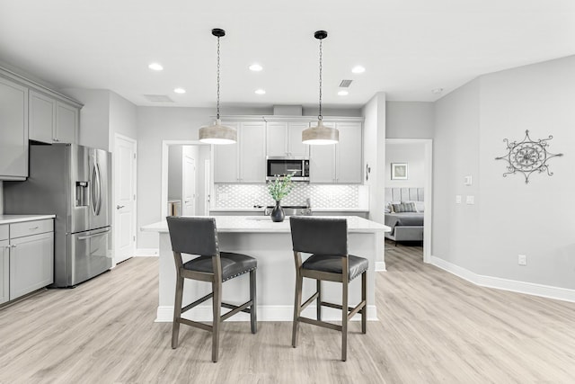 kitchen with pendant lighting, gray cabinetry, stainless steel appliances, a kitchen breakfast bar, and a center island with sink