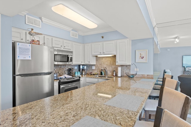 kitchen with appliances with stainless steel finishes, white cabinetry, a kitchen bar, decorative backsplash, and kitchen peninsula