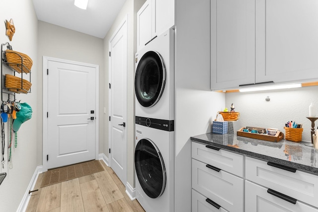 laundry room featuring cabinets, stacked washing maching and dryer, and light hardwood / wood-style flooring