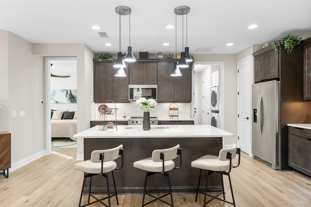 kitchen featuring dark brown cabinetry, stacked washer / dryer, an island with sink, and appliances with stainless steel finishes