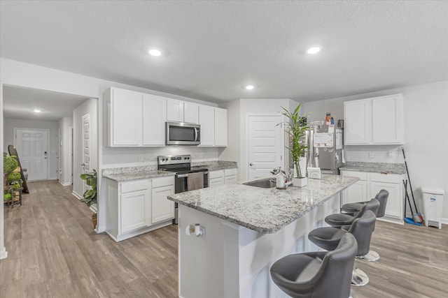 kitchen featuring sink, a kitchen island with sink, stainless steel appliances, light stone countertops, and white cabinets