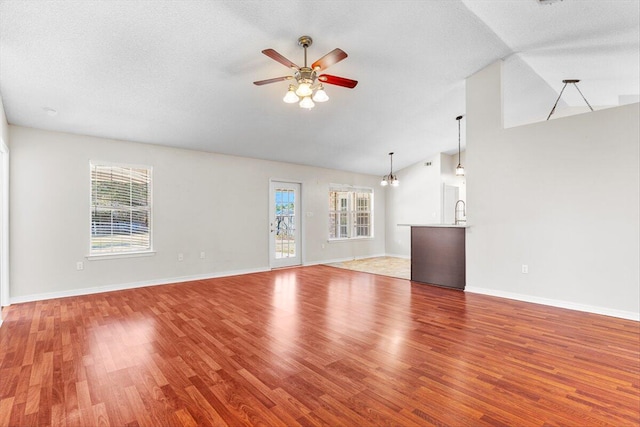 unfurnished living room with lofted ceiling, ceiling fan with notable chandelier, a textured ceiling, and hardwood / wood-style flooring