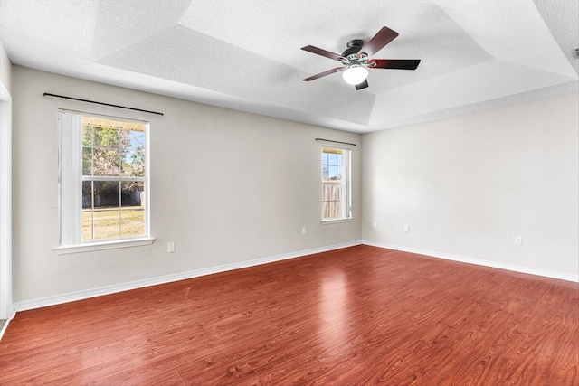 spare room with a tray ceiling, wood-type flooring, a textured ceiling, and ceiling fan