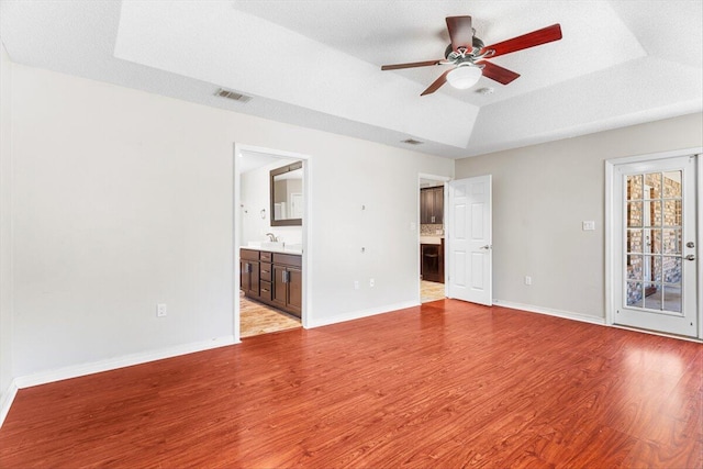 spare room featuring sink, ceiling fan, a tray ceiling, a textured ceiling, and light hardwood / wood-style flooring