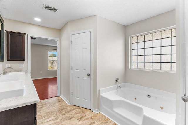 bathroom with vanity, a textured ceiling, and a tub to relax in