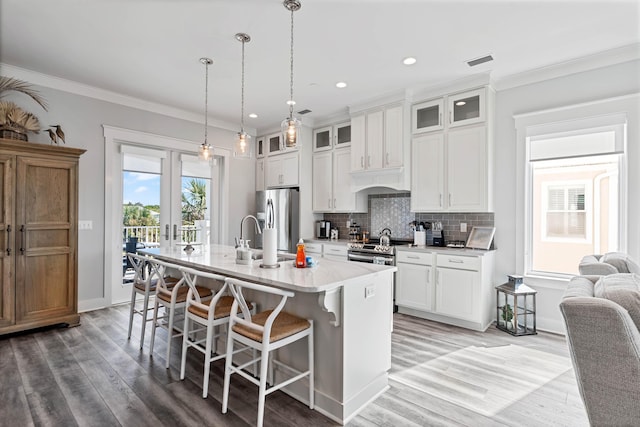 kitchen featuring white cabinetry, decorative light fixtures, appliances with stainless steel finishes, and a center island with sink