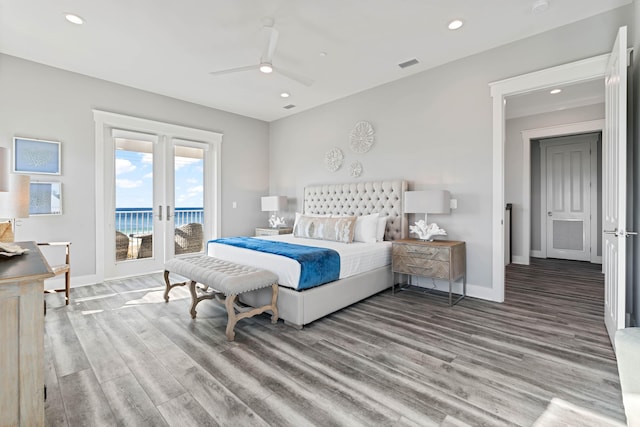 bedroom featuring access to exterior, hardwood / wood-style flooring, ceiling fan, and a water view