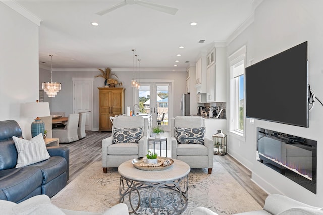 living room with crown molding, ceiling fan with notable chandelier, light hardwood / wood-style flooring, and french doors