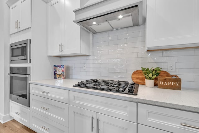 kitchen with stainless steel appliances, white cabinetry, light stone countertops, and wall chimney exhaust hood