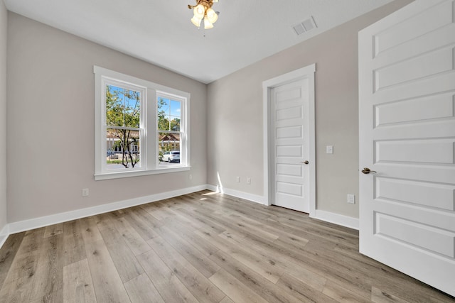 empty room featuring light wood-type flooring, visible vents, and baseboards