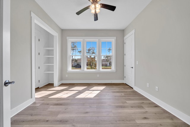 empty room featuring built in shelves, light hardwood / wood-style floors, and ceiling fan