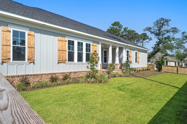 exterior space featuring brick siding, a shingled roof, board and batten siding, a front yard, and fence