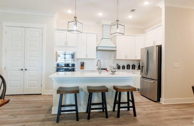 kitchen featuring premium range hood, white cabinetry, a center island with sink, pendant lighting, and stainless steel appliances