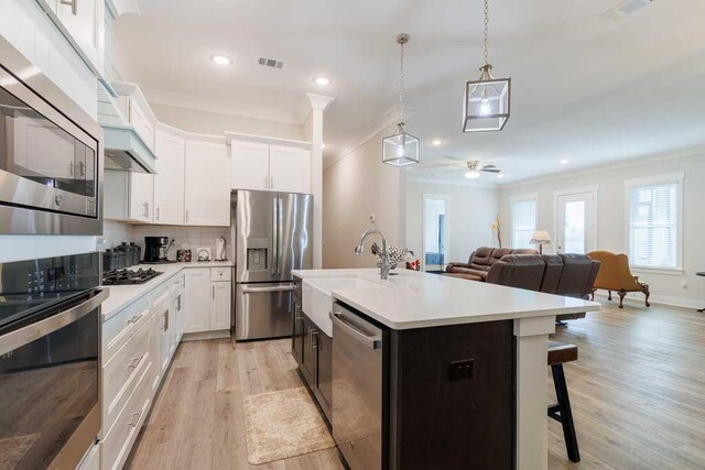 kitchen with stainless steel appliances, a kitchen island with sink, hanging light fixtures, and white cabinets