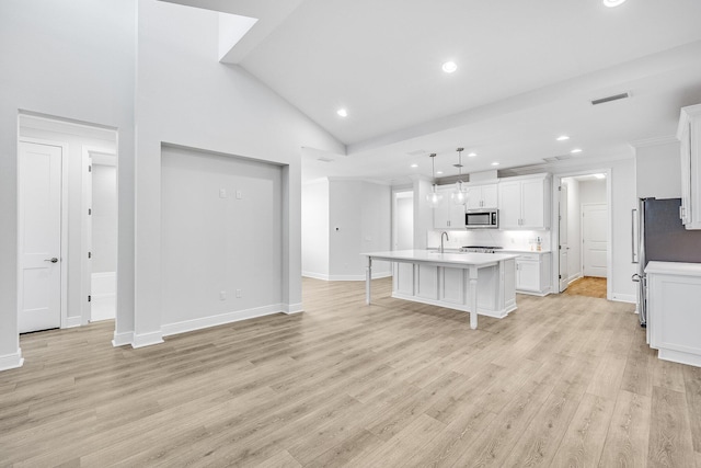 kitchen featuring pendant lighting, a breakfast bar area, light hardwood / wood-style floors, white cabinets, and a center island with sink