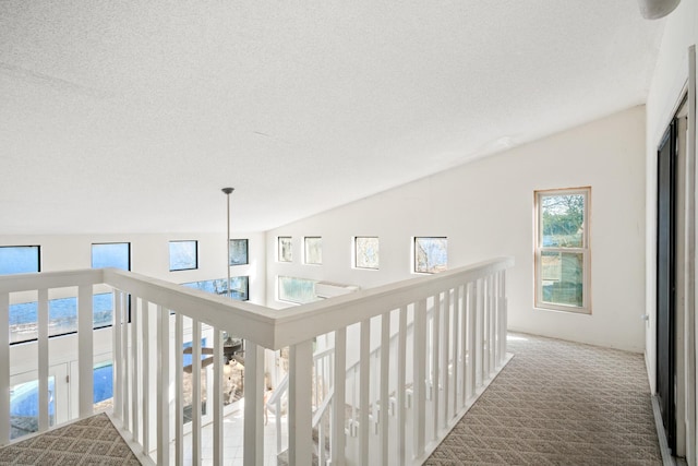 hallway with vaulted ceiling, a textured ceiling, and carpet