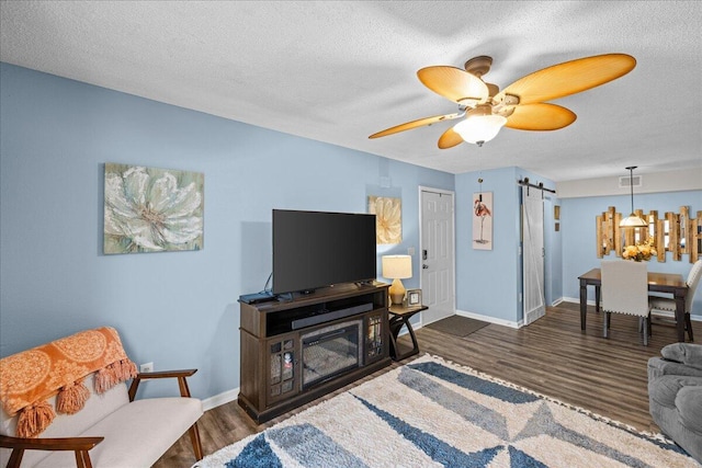 living room featuring ceiling fan, dark hardwood / wood-style floors, a barn door, and a textured ceiling