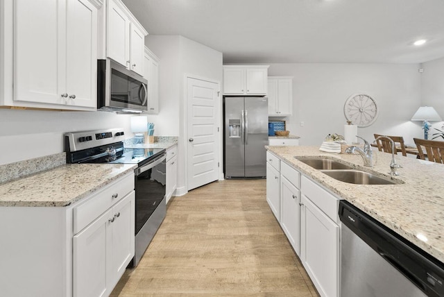 kitchen with appliances with stainless steel finishes, sink, white cabinets, light stone counters, and light hardwood / wood-style flooring