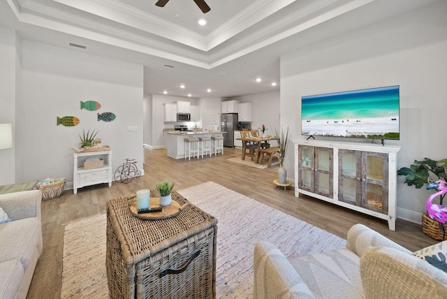 living room featuring hardwood / wood-style floors, ornamental molding, a raised ceiling, and ceiling fan