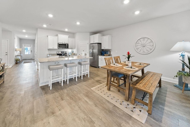 kitchen featuring white cabinetry, stainless steel appliances, a kitchen breakfast bar, light stone countertops, and a center island with sink