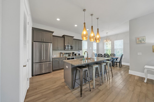 kitchen featuring sink, a breakfast bar area, stainless steel appliances, a center island with sink, and decorative light fixtures