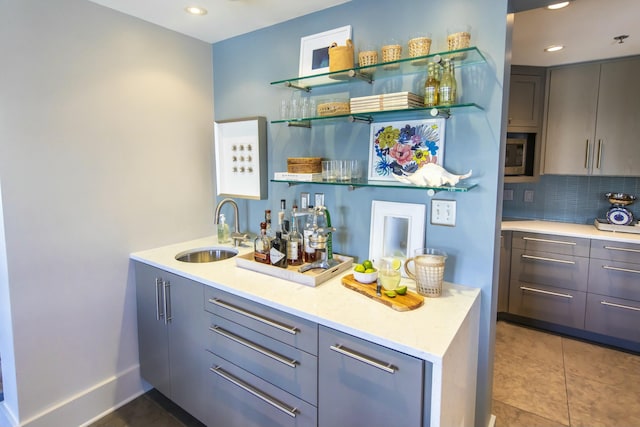 bar featuring tile patterned flooring, sink, backsplash, and gray cabinets