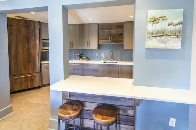 kitchen with sink, gray cabinetry, a kitchen breakfast bar, decorative backsplash, and light tile patterned floors