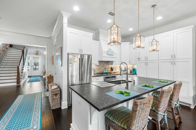 kitchen featuring sink, appliances with stainless steel finishes, white cabinetry, an island with sink, and decorative light fixtures