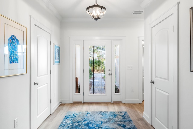 doorway with crown molding, a notable chandelier, and light wood-type flooring