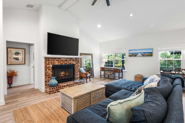 living room featuring high vaulted ceiling, light hardwood / wood-style flooring, beamed ceiling, ceiling fan, and a fireplace