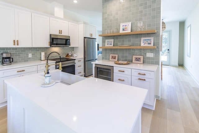 kitchen featuring wine cooler, white cabinetry, stainless steel appliances, light hardwood / wood-style floors, and backsplash