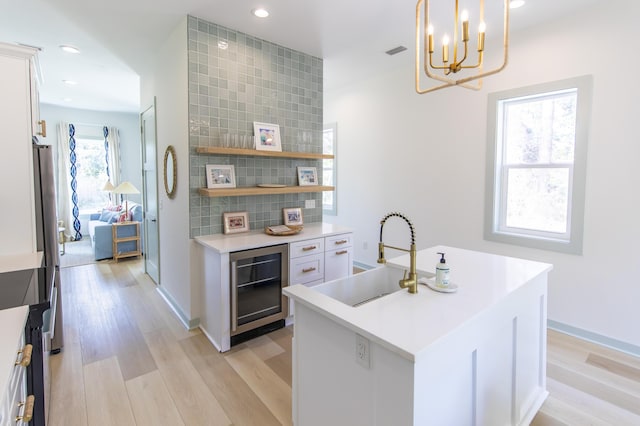 kitchen featuring sink, white cabinetry, wine cooler, a center island with sink, and decorative light fixtures