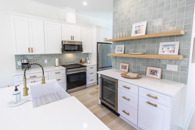 kitchen featuring light hardwood / wood-style flooring, appliances with stainless steel finishes, tasteful backsplash, white cabinets, and beverage cooler