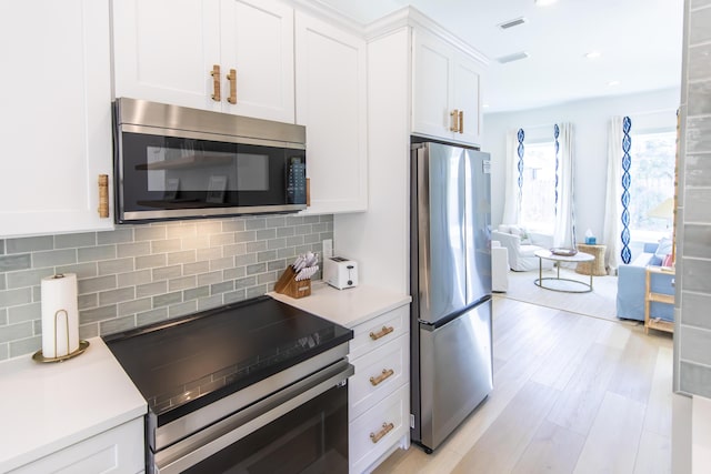 kitchen with stainless steel appliances, tasteful backsplash, white cabinets, and light wood-type flooring