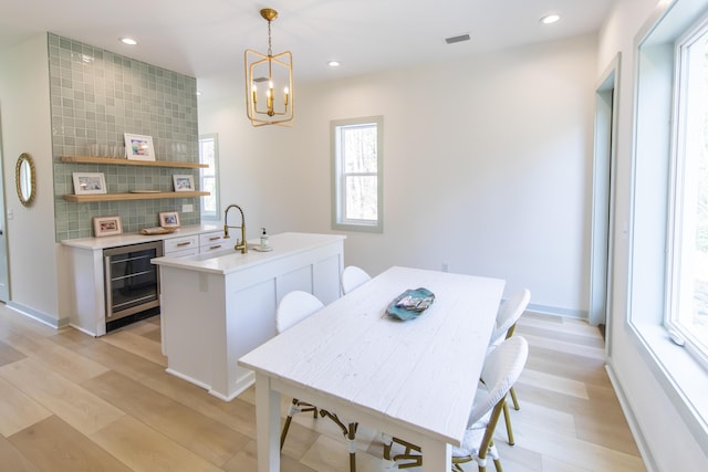 dining area featuring sink, an inviting chandelier, wine cooler, and light hardwood / wood-style floors